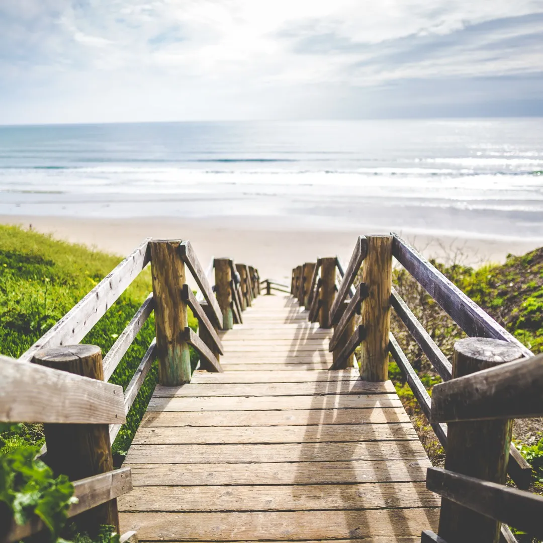 Escaliers en bois menant à une plage ensoleillée.