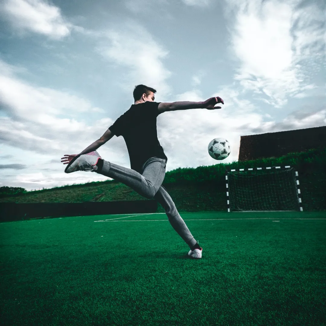 Un joueur de football concentré exécutant un coup de pied puissant sur un terrain verdoyant sous un ciel spectaculaire.